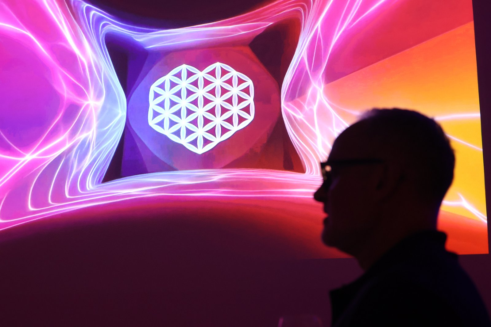 A visitor is silhouetted before the vivid geometric projection of Lumaform II.